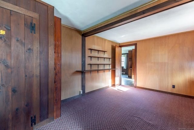 carpeted spare room featuring baseboards, beamed ceiling, and wooden walls