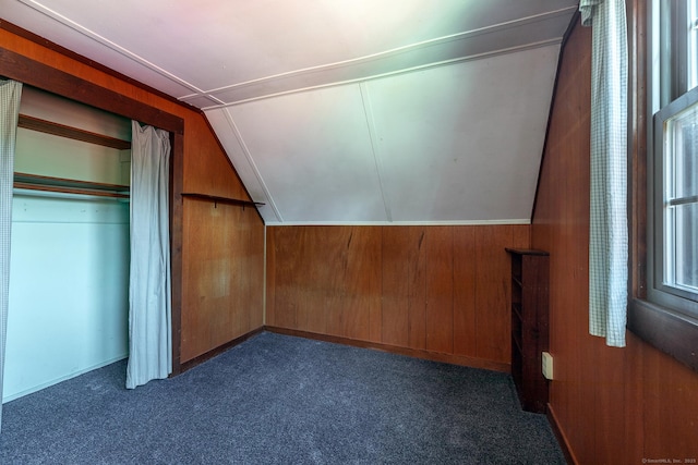 bonus room featuring dark carpet, lofted ceiling, and wooden walls