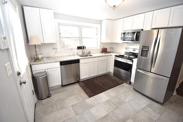 kitchen with light tile patterned flooring, appliances with stainless steel finishes, sink, white cabinets, and light stone countertops