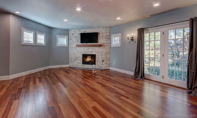 unfurnished living room with hardwood / wood-style floors and a stone fireplace
