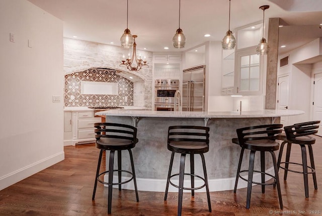 kitchen with dark wood-type flooring, a breakfast bar, white cabinetry, appliances with stainless steel finishes, and pendant lighting