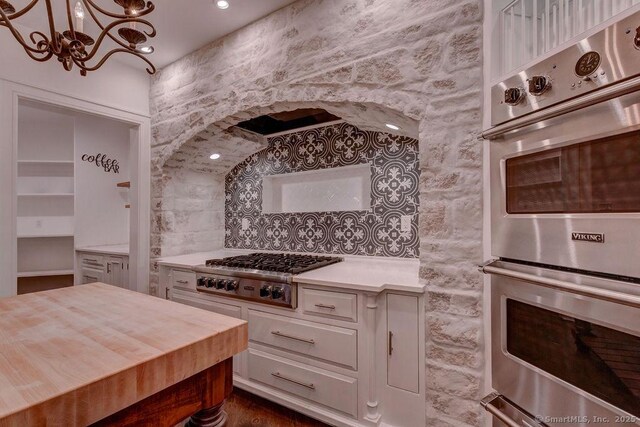 kitchen featuring stainless steel appliances, white cabinetry, hanging light fixtures, and a notable chandelier