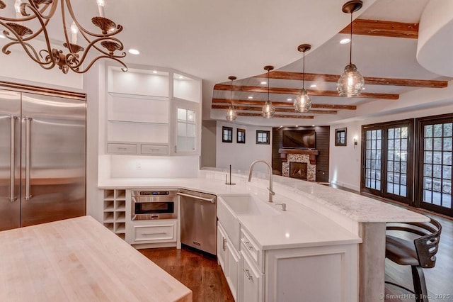 kitchen with appliances with stainless steel finishes, pendant lighting, beamed ceiling, sink, and white cabinets