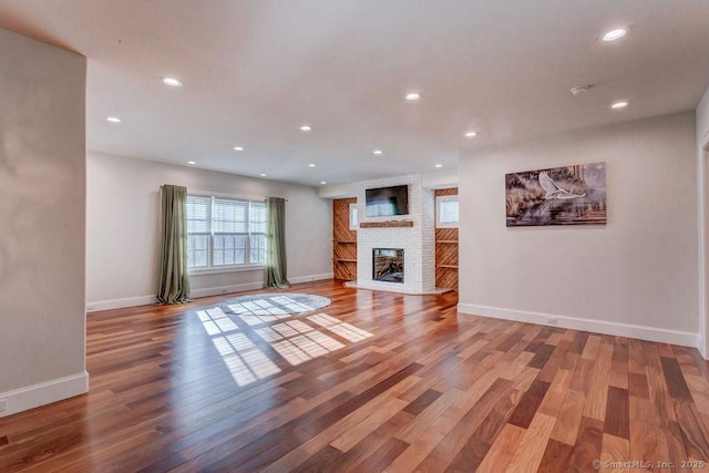 unfurnished living room with wood-type flooring and a brick fireplace