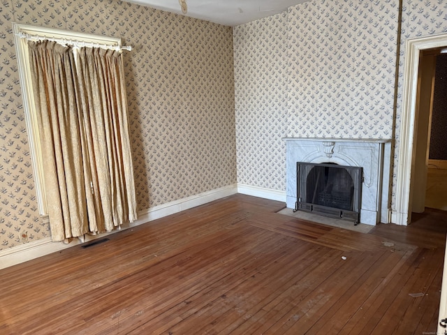 unfurnished living room with a high end fireplace, wood finished floors, baseboards, and wallpapered walls