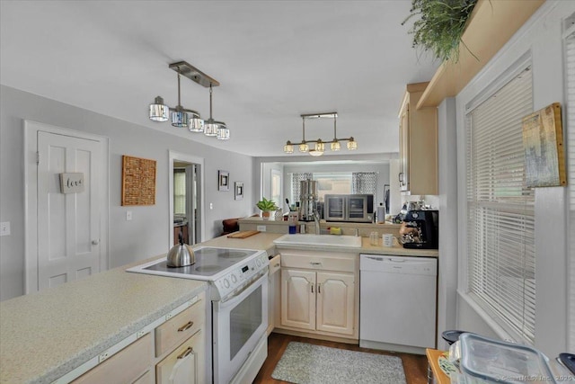 kitchen with decorative light fixtures, light countertops, a sink, white appliances, and a peninsula