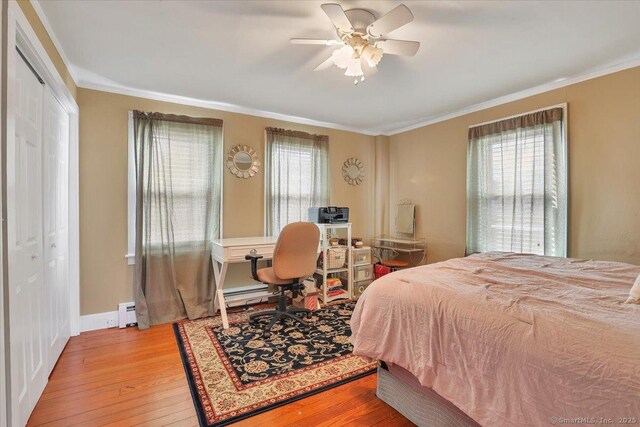 bedroom with baseboards, ornamental molding, light wood-type flooring, a baseboard heating unit, and a closet