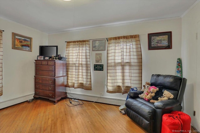 sitting room featuring a baseboard heating unit, wood-type flooring, baseboards, and crown molding