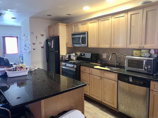 kitchen featuring stainless steel appliances, light brown cabinetry, sink, and dark stone countertops