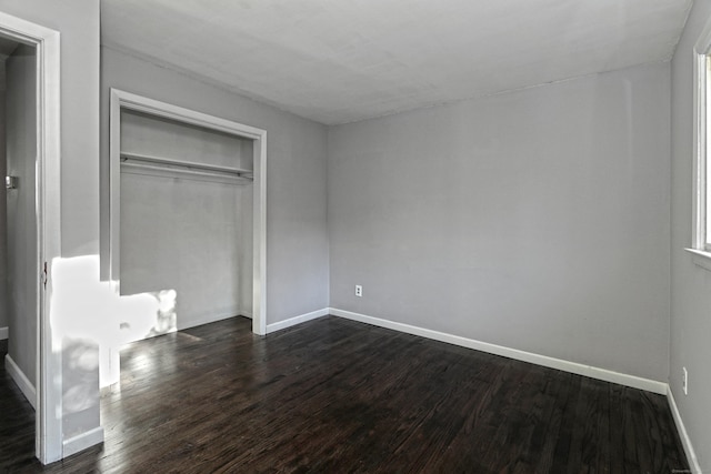 unfurnished bedroom with a closet, dark wood finished floors, and baseboards