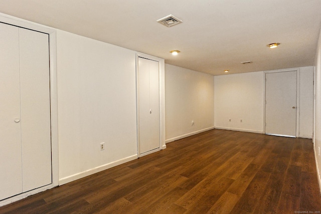 unfurnished bedroom featuring multiple closets, baseboards, visible vents, and wood finished floors