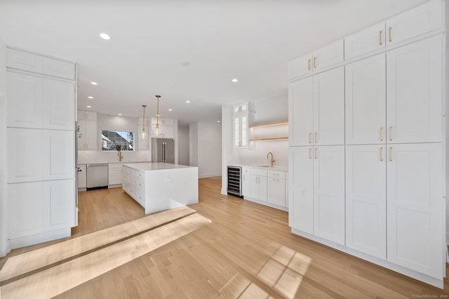 kitchen featuring a kitchen island, appliances with stainless steel finishes, white cabinets, beverage cooler, and hanging light fixtures