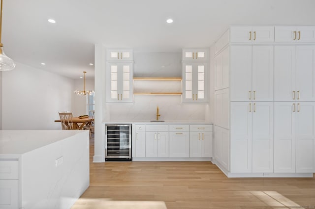 bar with wine cooler, pendant lighting, white cabinets, and light wood-type flooring