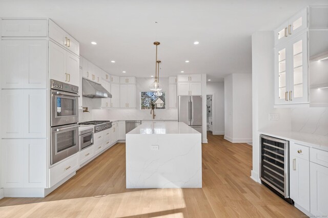 kitchen with appliances with stainless steel finishes, white cabinets, beverage cooler, hanging light fixtures, and a center island