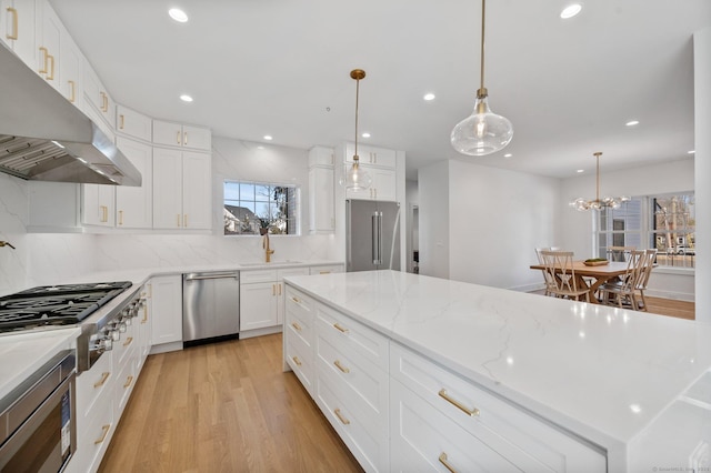 kitchen with sink, appliances with stainless steel finishes, white cabinetry, hanging light fixtures, and light hardwood / wood-style floors