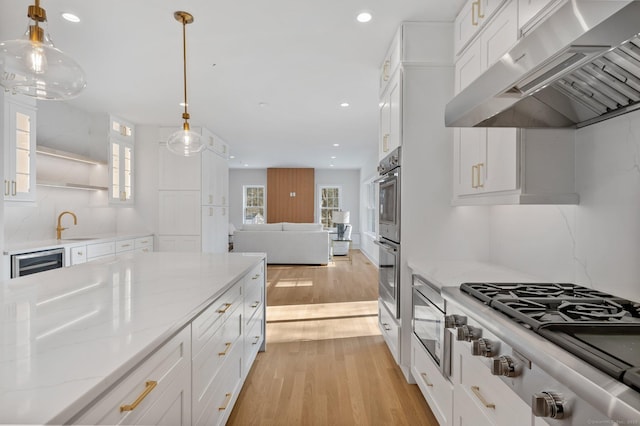 kitchen with hanging light fixtures, wall chimney range hood, beverage cooler, light stone countertops, and white cabinets