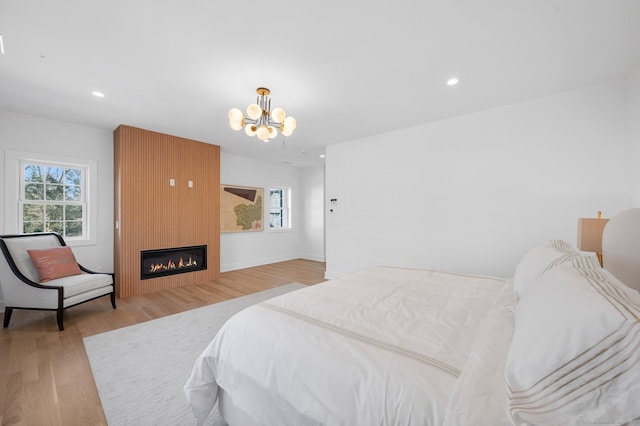 bedroom with a large fireplace, a chandelier, and light hardwood / wood-style floors