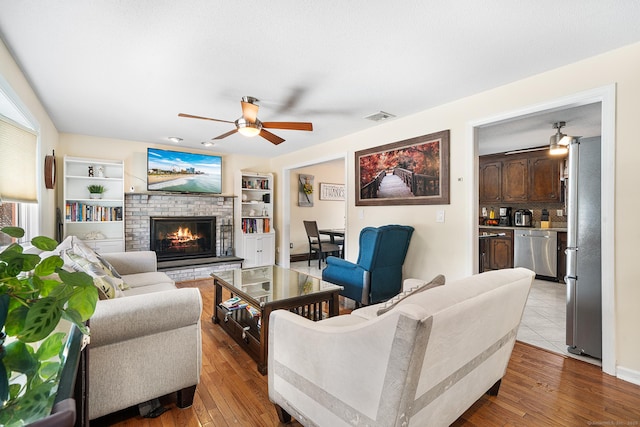 living room with a brick fireplace, ceiling fan, and light hardwood / wood-style flooring