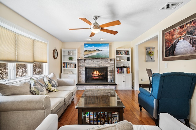 living room featuring a brick fireplace, wood-type flooring, and ceiling fan