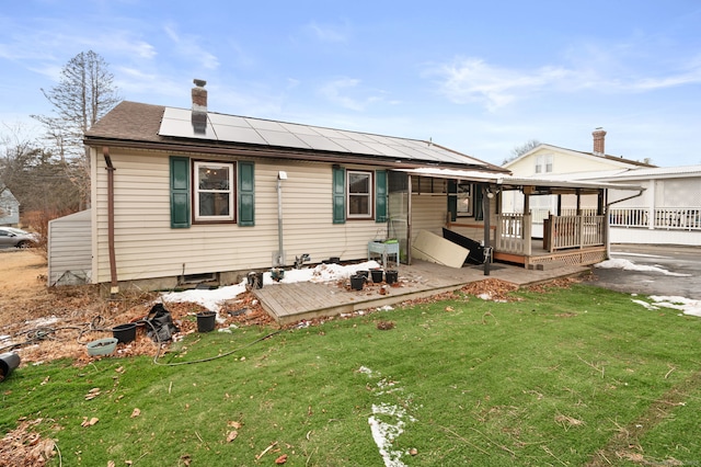 rear view of property with a wooden deck, a yard, and solar panels