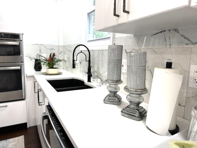 kitchen with dishwashing machine, sink, white cabinetry, double oven, and tasteful backsplash