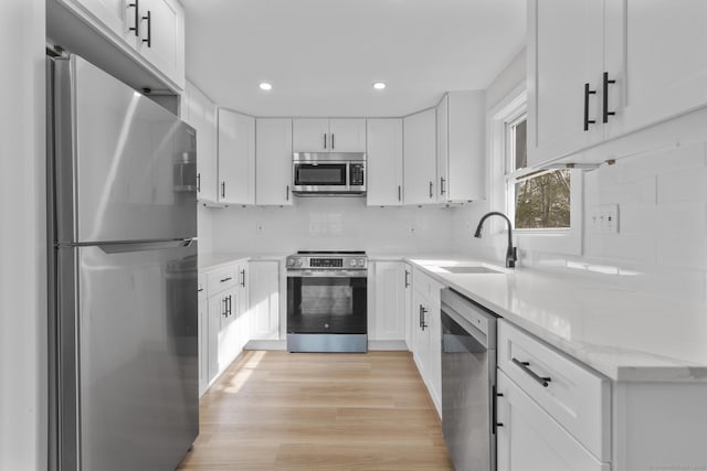 kitchen with light wood finished floors, recessed lighting, a sink, stainless steel appliances, and white cabinets