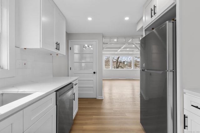 kitchen with light wood-style floors, white cabinets, stainless steel dishwasher, backsplash, and freestanding refrigerator