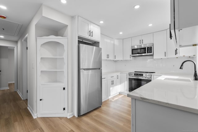 kitchen featuring light stone counters, stainless steel appliances, light wood-style floors, white cabinetry, and a sink