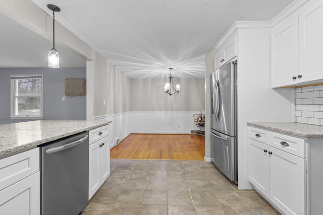 kitchen with white cabinetry, decorative light fixtures, a wainscoted wall, and appliances with stainless steel finishes