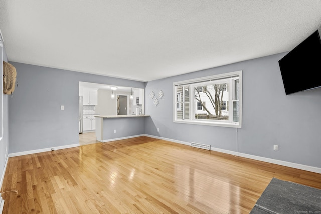 unfurnished living room featuring visible vents, light wood-type flooring, and baseboards