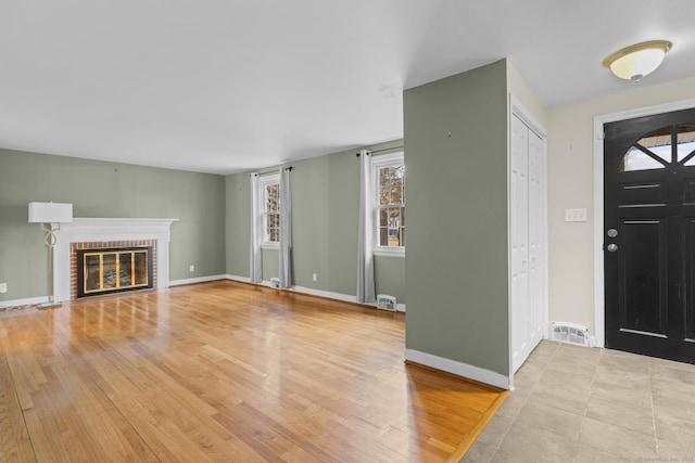 entryway with visible vents, baseboards, light wood-style floors, and a brick fireplace