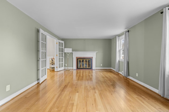 unfurnished living room with a brick fireplace, light wood-style flooring, and baseboards