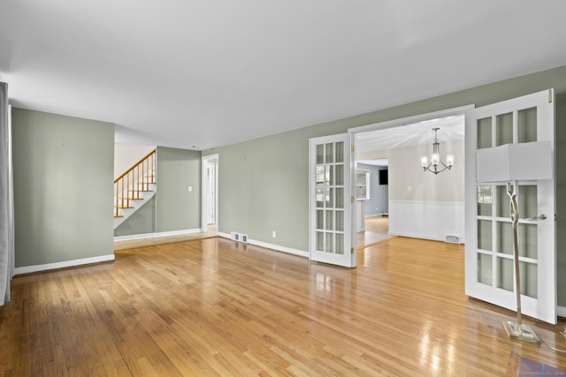 spare room featuring visible vents, baseboards, light wood-type flooring, stairs, and a notable chandelier