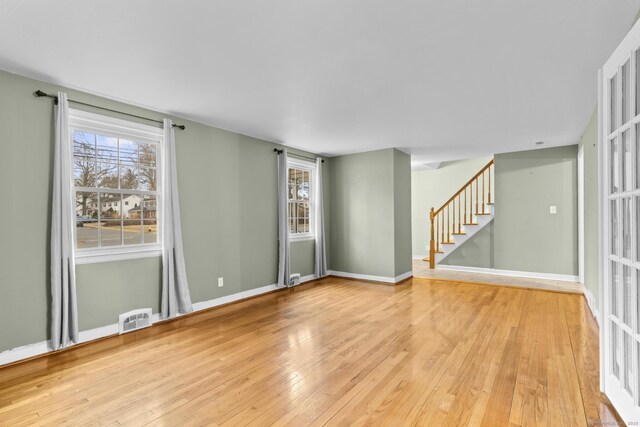 unfurnished room with stairway, baseboards, visible vents, and light wood finished floors