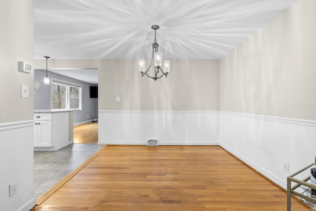 unfurnished dining area with visible vents, baseboards, a chandelier, and light wood finished floors