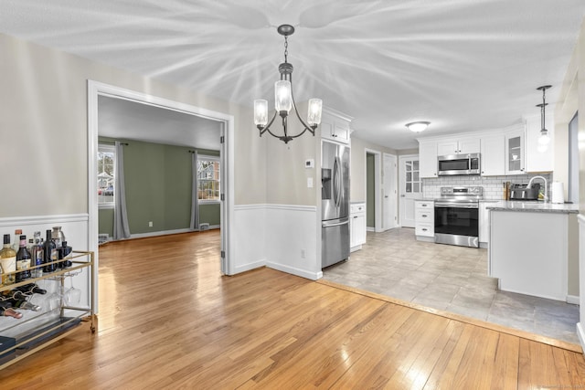 kitchen featuring light wood-type flooring, tasteful backsplash, white cabinetry, stainless steel appliances, and glass insert cabinets