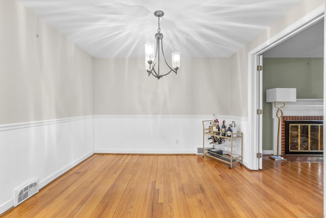 unfurnished dining area featuring an inviting chandelier, a brick fireplace, wood finished floors, and visible vents