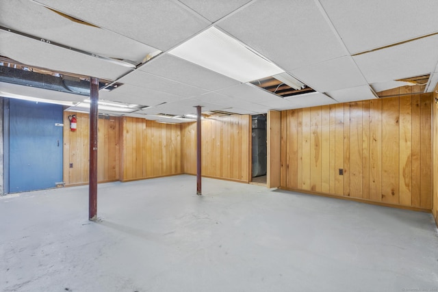 finished basement featuring a paneled ceiling and wooden walls