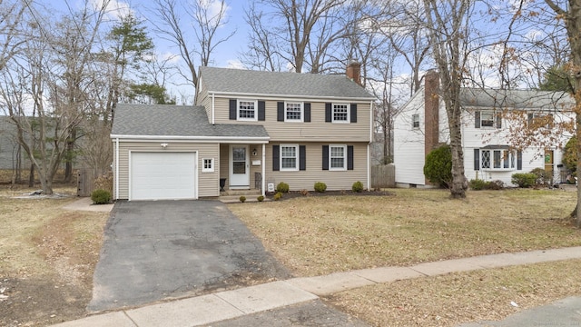 colonial house with a front lawn, aphalt driveway, a shingled roof, a garage, and a chimney