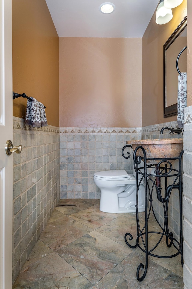 bathroom with toilet and tile walls