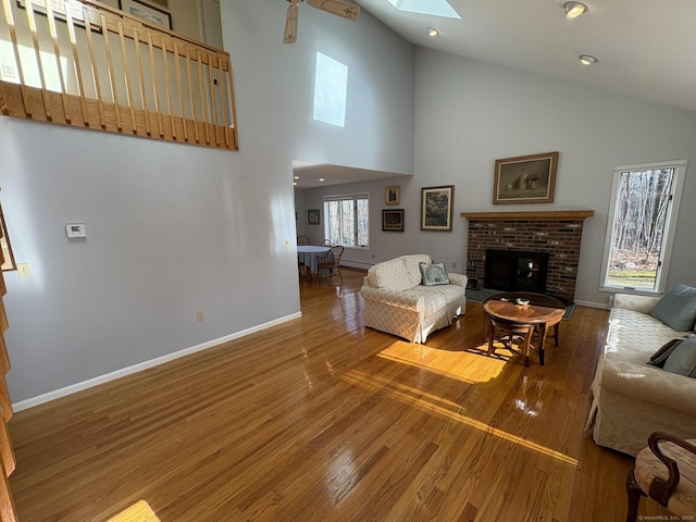 living room with wood-type flooring, high vaulted ceiling, a fireplace, and a skylight