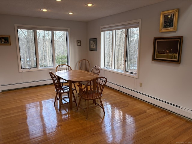 dining area with a wealth of natural light, baseboard heating, and light hardwood / wood-style floors