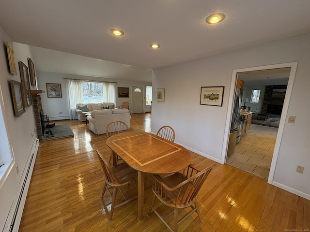 dining area featuring baseboard heating, a fireplace, and light hardwood / wood-style floors