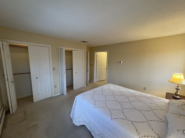 bedroom featuring a baseboard heating unit, two closets, and light colored carpet