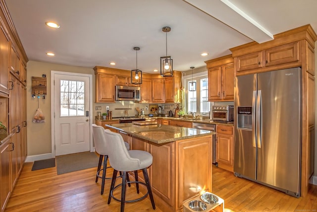 kitchen with sink, hanging light fixtures, stainless steel appliances, a kitchen island, and dark stone counters