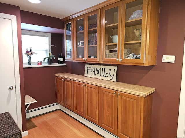 bar with tile counters, light hardwood / wood-style floors, and a baseboard radiator