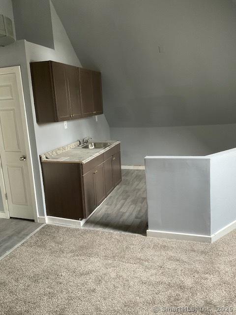 kitchen with dark brown cabinets, sink, lofted ceiling, and light wood-type flooring