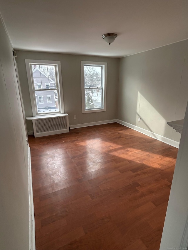 spare room featuring dark wood-type flooring, radiator heating unit, and a wealth of natural light