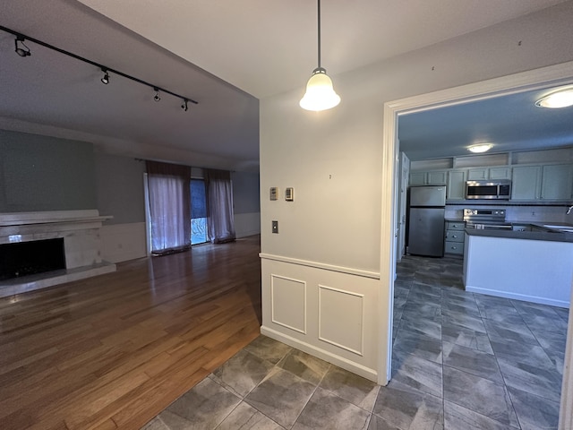 kitchen with appliances with stainless steel finishes, rail lighting, sink, hanging light fixtures, and dark wood-type flooring