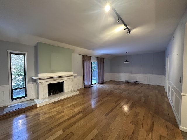 unfurnished living room with track lighting, hardwood / wood-style floors, a tile fireplace, and a wealth of natural light